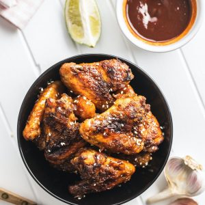 Grilled chicken wings in bowl with BBQ sauce.